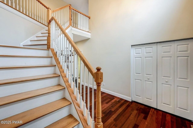 staircase with a high ceiling, baseboards, and wood finished floors