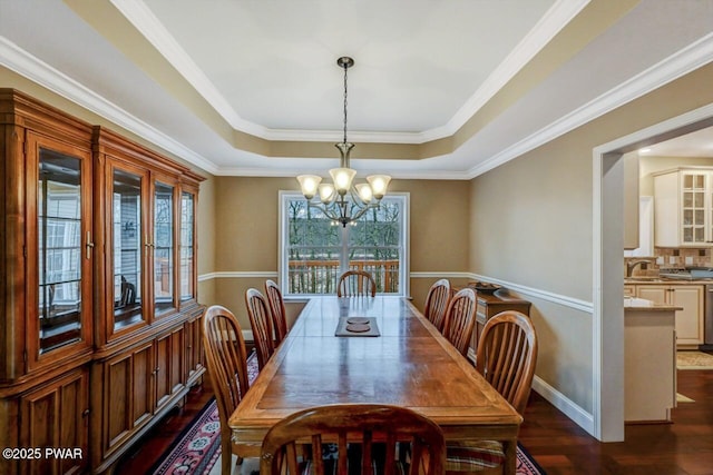 dining area featuring a notable chandelier, dark wood-type flooring, baseboards, a tray ceiling, and crown molding