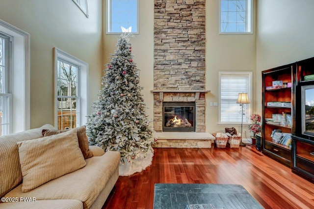 living area with a stone fireplace, wood finished floors, and a high ceiling