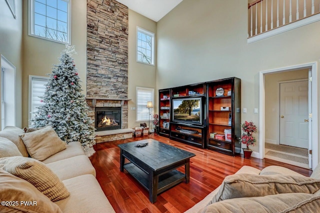 living room featuring a stone fireplace, baseboards, and wood finished floors