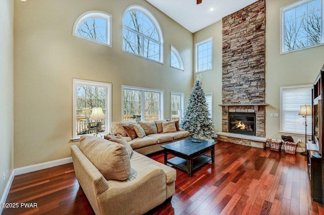 living room featuring dark wood-style flooring, a high ceiling, a stone fireplace, and baseboards