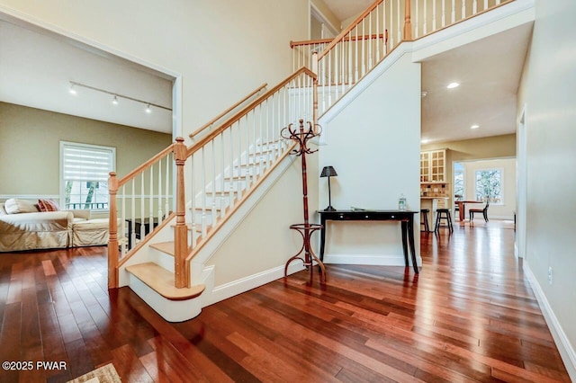 staircase with hardwood / wood-style floors, a high ceiling, a wealth of natural light, and baseboards