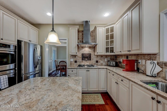 kitchen featuring dark wood-style floors, stainless steel appliances, decorative backsplash, glass insert cabinets, and wall chimney range hood