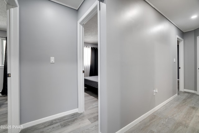 hallway featuring light wood-style floors, baseboards, and a textured ceiling