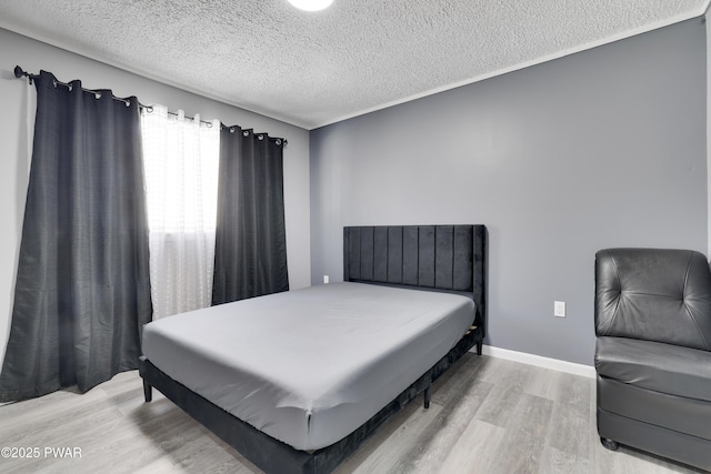 bedroom featuring a textured ceiling, baseboards, and wood finished floors