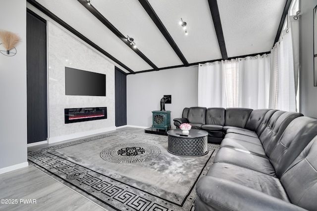 living room with lofted ceiling with beams, a textured ceiling, baseboards, light wood finished floors, and a wood stove