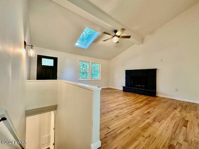 unfurnished living room featuring a fireplace, ceiling fan, vaulted ceiling with skylight, and hardwood / wood-style flooring