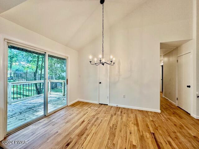 unfurnished dining area with hardwood / wood-style floors, vaulted ceiling, and a notable chandelier