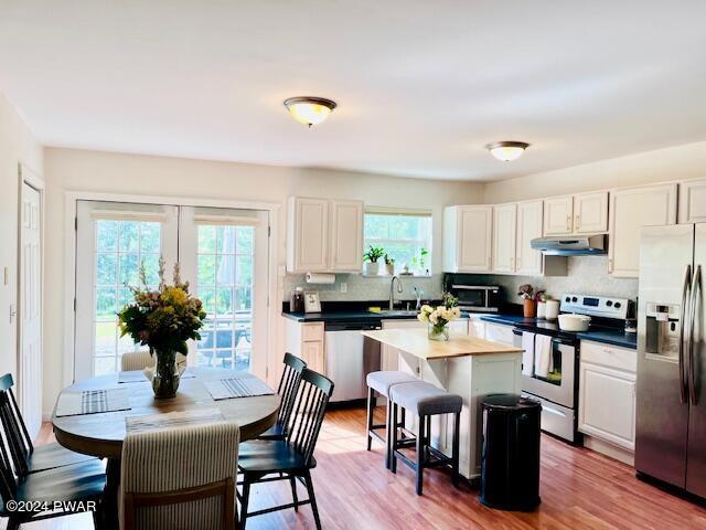 kitchen featuring stainless steel appliances, sink, white cabinets, hardwood / wood-style floors, and a center island