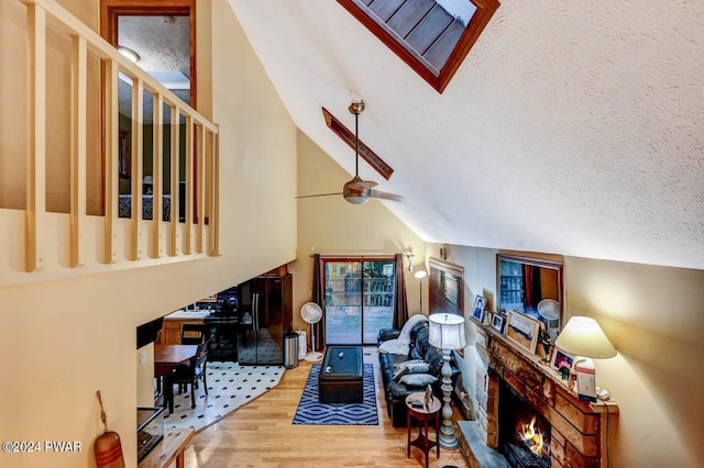 living room with ceiling fan, hardwood / wood-style floors, high vaulted ceiling, and a textured ceiling