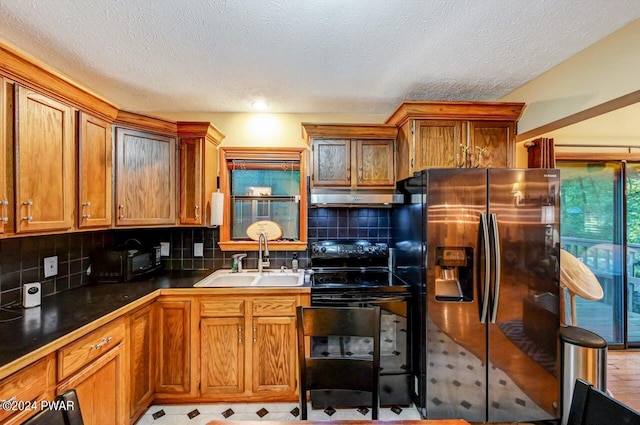 kitchen featuring decorative backsplash, stainless steel refrigerator with ice dispenser, black range with electric cooktop, a textured ceiling, and sink