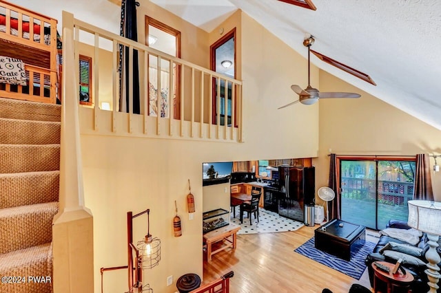 living room with a textured ceiling, hardwood / wood-style flooring, high vaulted ceiling, and ceiling fan