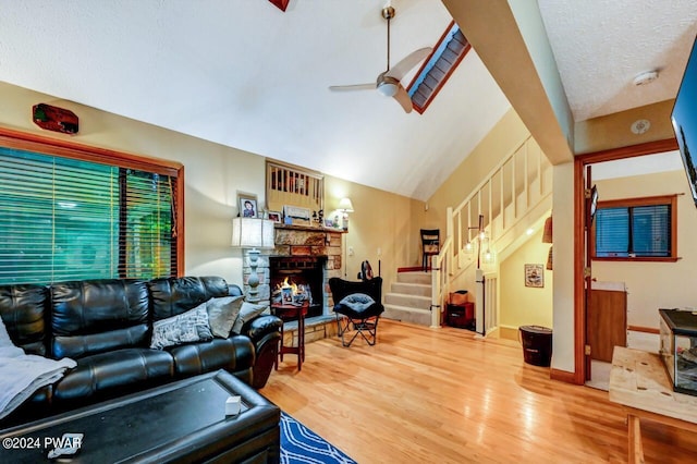 living room featuring ceiling fan, a stone fireplace, wood-type flooring, a textured ceiling, and lofted ceiling