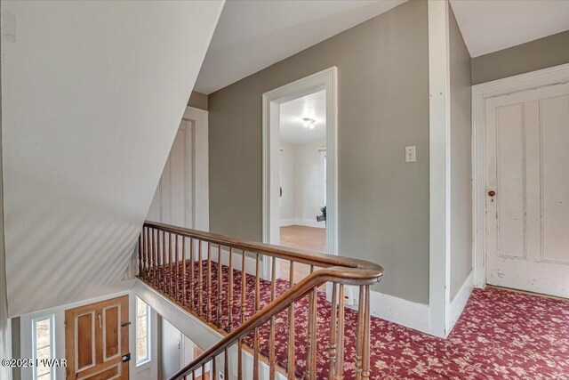 hall featuring baseboards, carpet flooring, and an upstairs landing