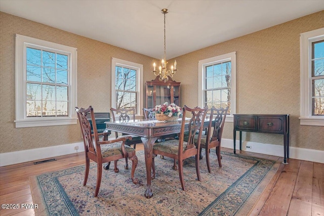 dining space with a notable chandelier, visible vents, baseboards, and hardwood / wood-style flooring
