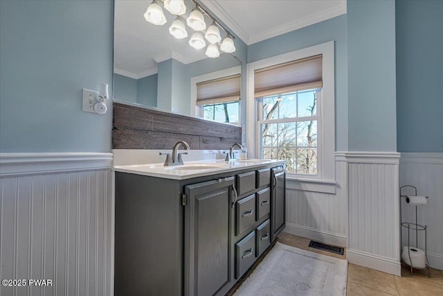 bathroom with crown molding, wainscoting, double vanity, and a sink