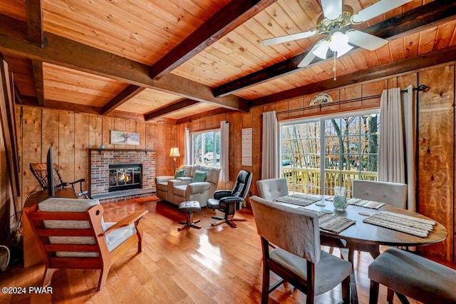 dining room featuring beam ceiling, wood walls, light hardwood / wood-style floors, a fireplace, and wood ceiling