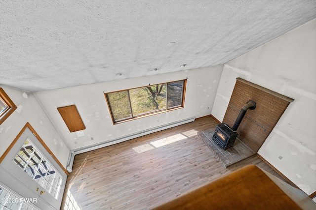 unfurnished living room with a textured ceiling, wood finished floors, a wood stove, and a baseboard radiator