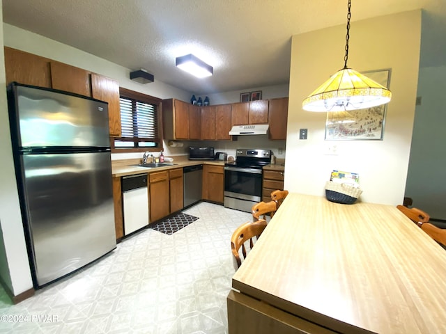 kitchen featuring appliances with stainless steel finishes, a textured ceiling, decorative light fixtures, and sink