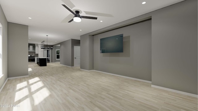 unfurnished living room featuring ceiling fan with notable chandelier and light hardwood / wood-style flooring