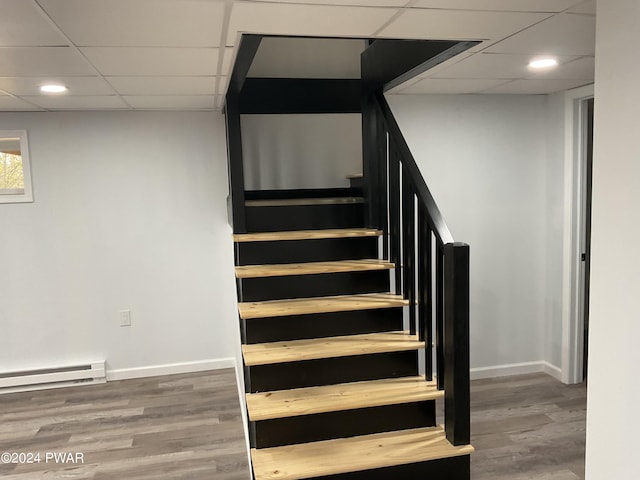 staircase with wood-type flooring, a baseboard radiator, and a drop ceiling