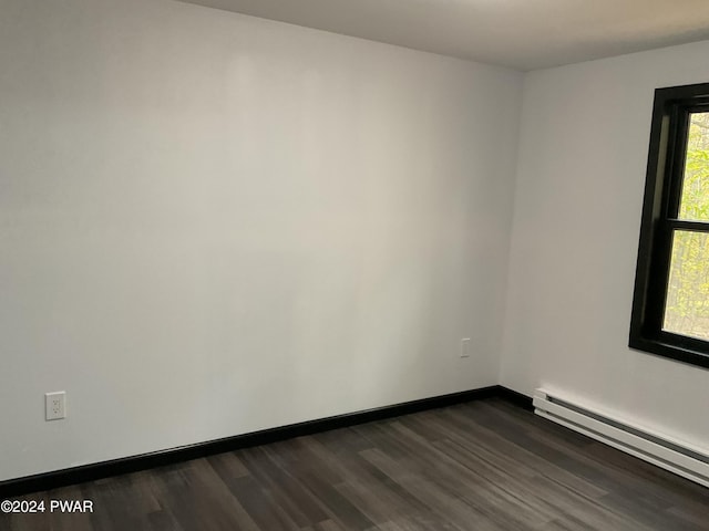 empty room with a healthy amount of sunlight, dark wood-type flooring, and a baseboard heating unit