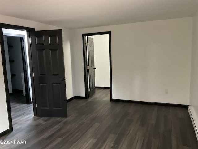 empty room featuring a baseboard heating unit and dark wood-type flooring