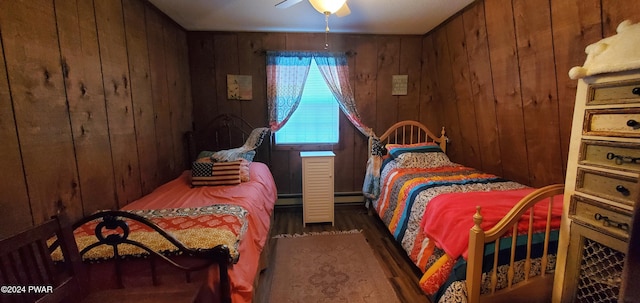 bedroom with ceiling fan, a baseboard radiator, dark hardwood / wood-style flooring, and wood walls