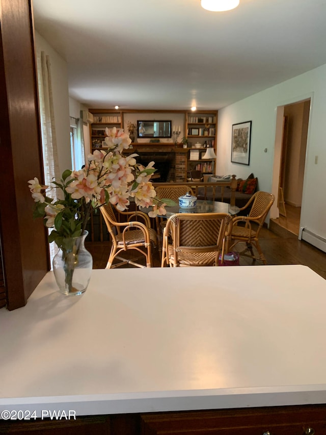 dining room featuring built in shelves, dark hardwood / wood-style floors, a fireplace, and a baseboard heating unit