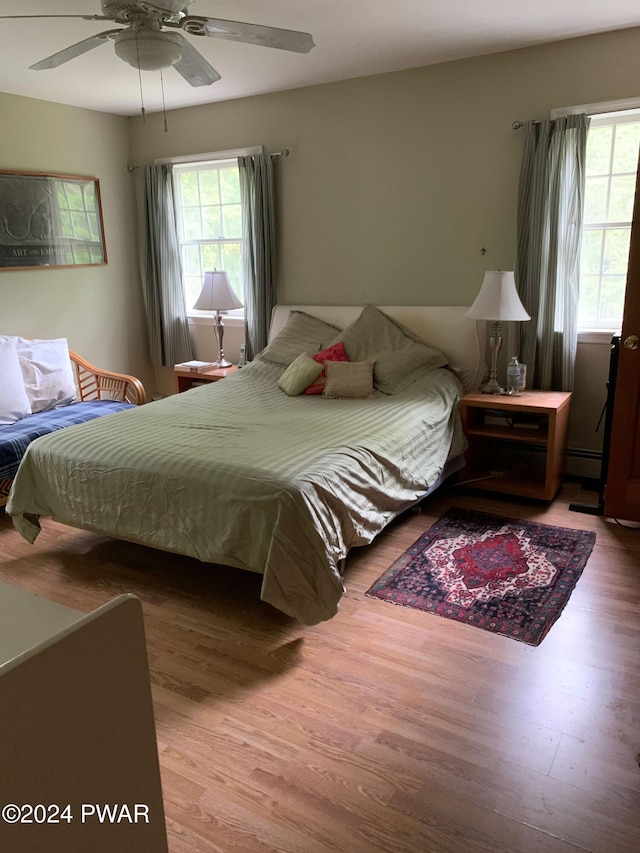 bedroom with hardwood / wood-style floors, ceiling fan, and baseboard heating