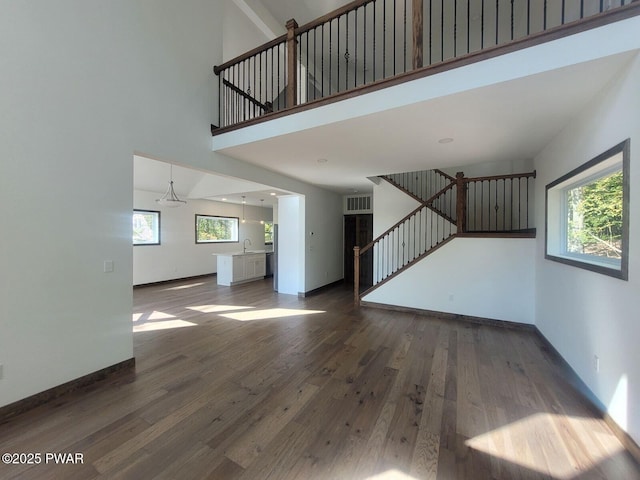 unfurnished living room featuring a high ceiling, dark hardwood / wood-style flooring, a notable chandelier, and sink