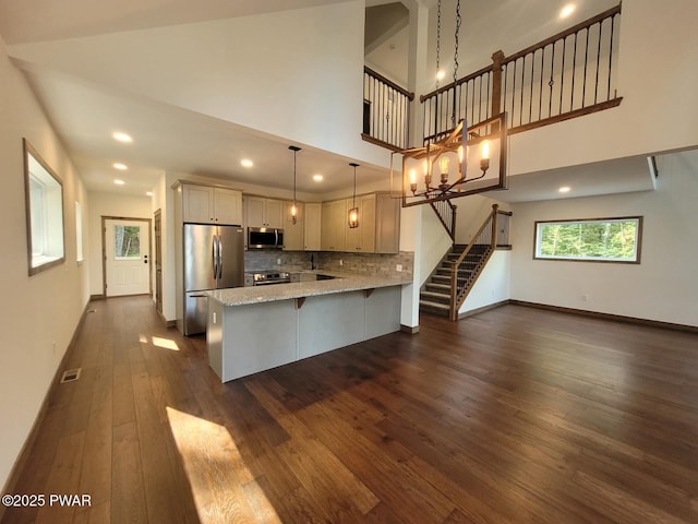 kitchen featuring hanging light fixtures, stainless steel appliances, light stone counters, kitchen peninsula, and decorative backsplash