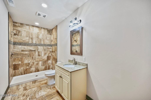 bathroom featuring a tile shower, vanity, and toilet