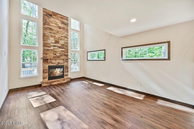 unfurnished living room featuring a stone fireplace, wood-type flooring, and a wealth of natural light