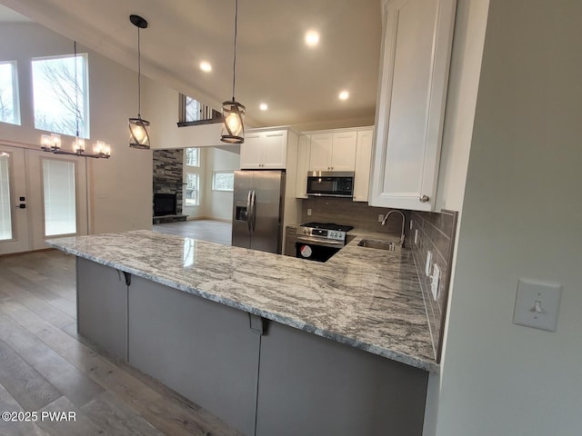 kitchen featuring kitchen peninsula, appliances with stainless steel finishes, sink, decorative light fixtures, and white cabinets