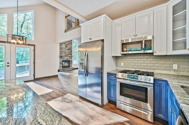 kitchen with light stone countertops, appliances with stainless steel finishes, tasteful backsplash, blue cabinetry, and white cabinetry