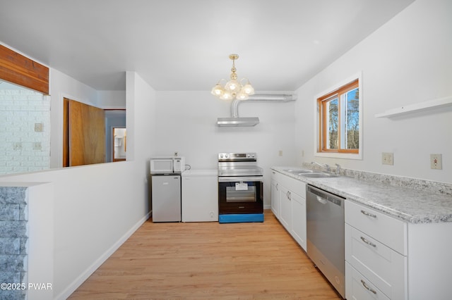 kitchen with appliances with stainless steel finishes, white cabinetry, sink, hanging light fixtures, and light hardwood / wood-style flooring