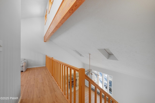 hallway with beamed ceiling, a skylight, light hardwood / wood-style flooring, and a textured ceiling