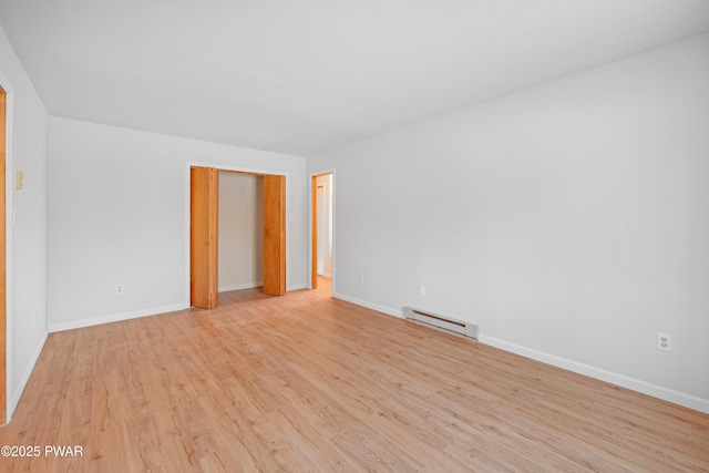 unfurnished room featuring a baseboard heating unit and light wood-type flooring