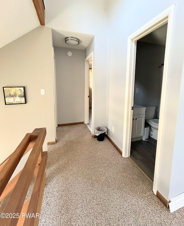 hall featuring baseboards, lofted ceiling, and carpet