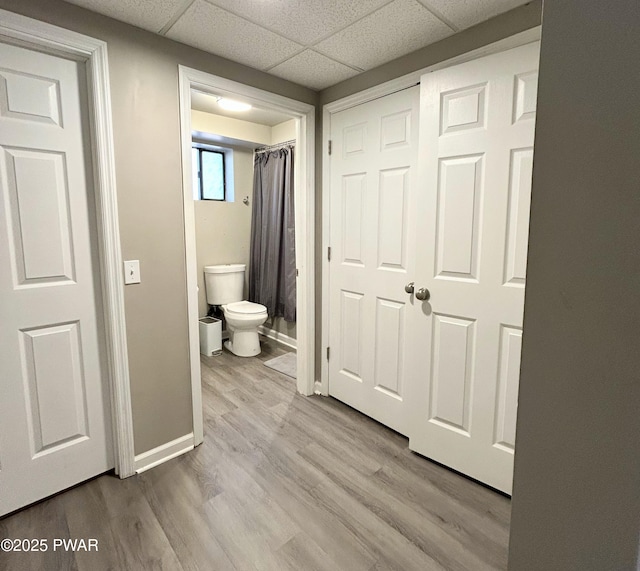 bathroom with a drop ceiling, toilet, baseboards, and wood finished floors