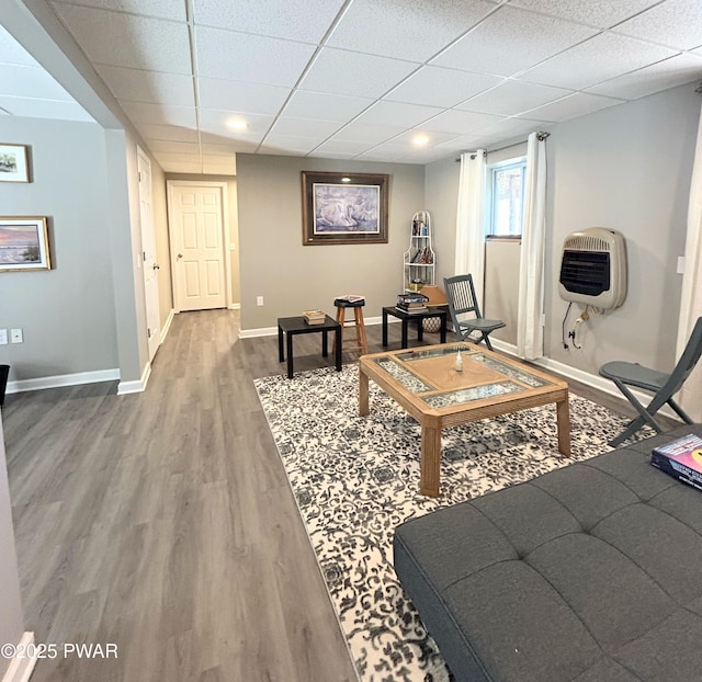 living room with heating unit, wood finished floors, baseboards, and a paneled ceiling