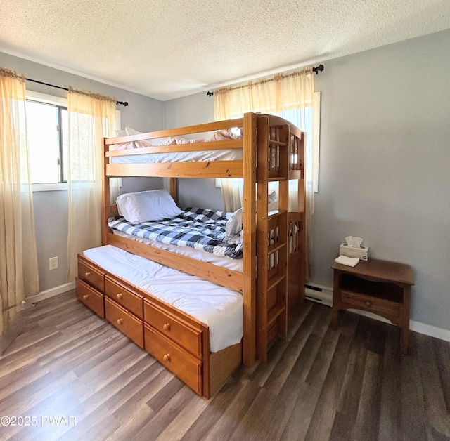 bedroom with a baseboard heating unit, baseboards, a textured ceiling, and wood finished floors