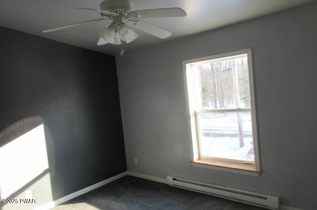 empty room featuring a baseboard heating unit, ceiling fan, and dark colored carpet