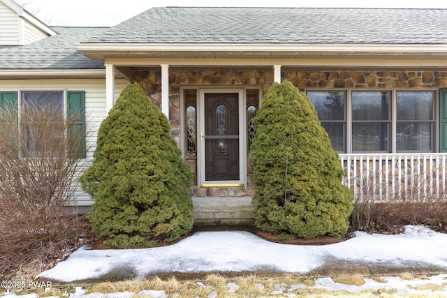 snow covered property entrance featuring roof with shingles