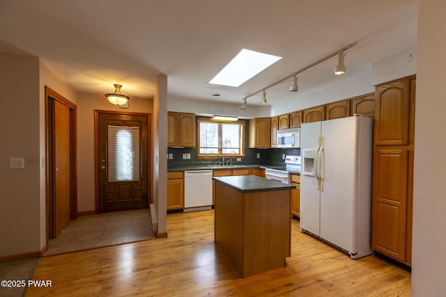 kitchen with a skylight, dark countertops, a sink, light wood-type flooring, and white appliances