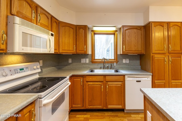 kitchen with white appliances, brown cabinetry, and a sink