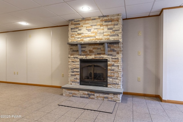 unfurnished living room with a stone fireplace, a paneled ceiling, and baseboards