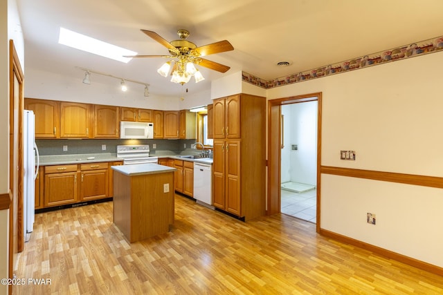 kitchen featuring white appliances, a skylight, a kitchen island, a sink, and decorative backsplash