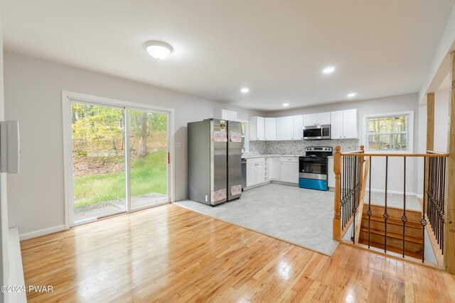 kitchen with backsplash, light wood-type flooring, a wealth of natural light, appliances with stainless steel finishes, and white cabinetry